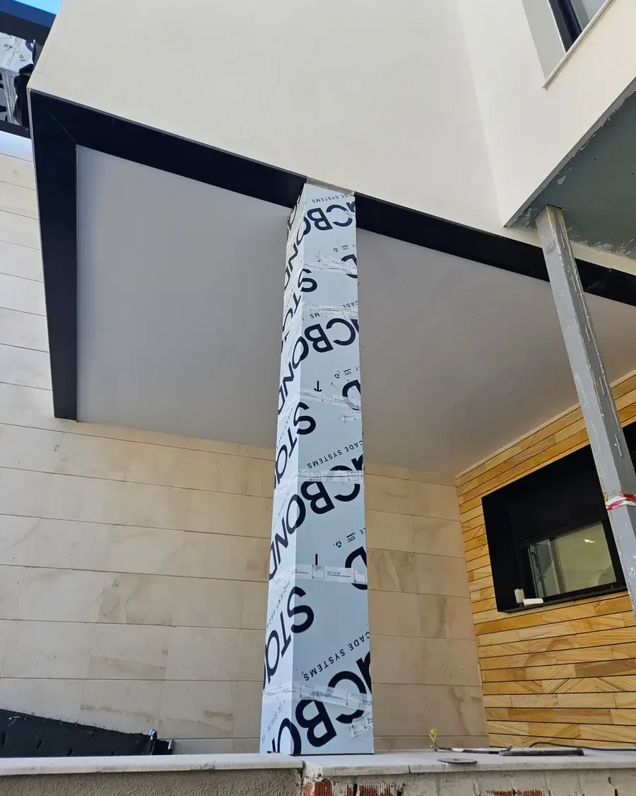 Detalle de fachada con porcelánico, madera y panel de aluminio protegido durante la obra