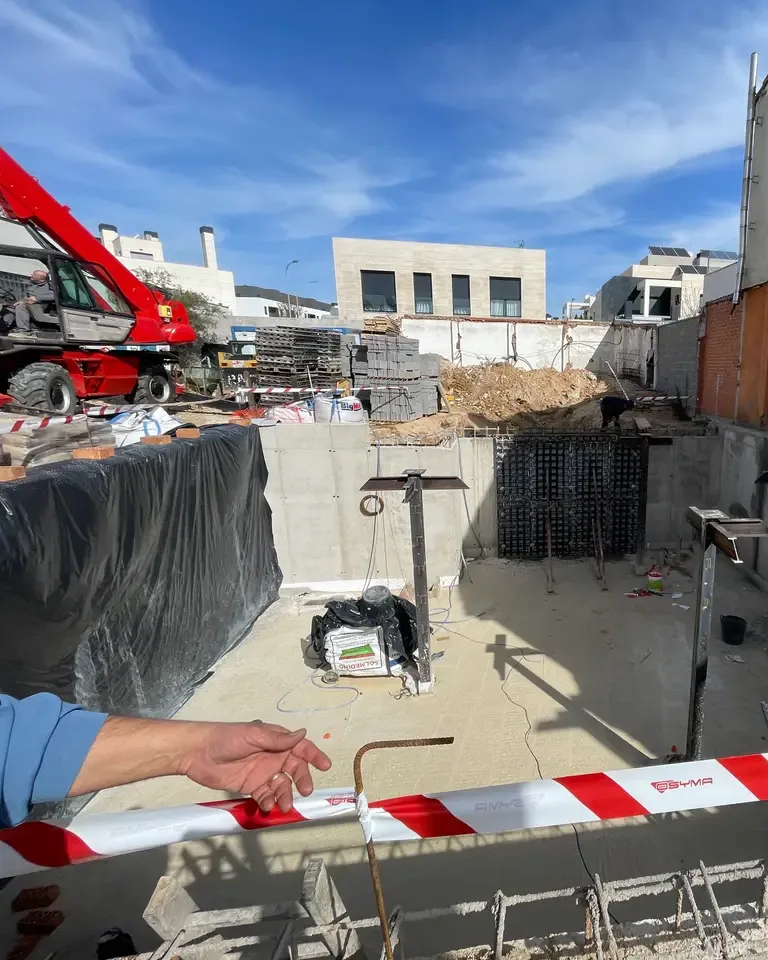 Mano junto a un armado y a la cinta de balizamiento en la cimentación de una obra